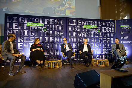 Von links nach rechts sitzen Daniel Krupka, Lea Schönberger, Lars Bernard, Martin Wolf und Florian Tschorsch auf der Bühne. Lars Bernard spricht in ein Mikrofon, während die anderen zuhören. Im Hintergrund stehen violette Banner mit dem Festival-Logo und dem Schriftzug „Digital Resilience“.