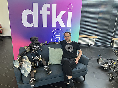 Gereon Rahnfeld next to a robot on a sofa at DFKI